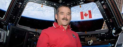 Chris Hadfield poses with the Canadian flag in the Cupola module of the International Space Station.