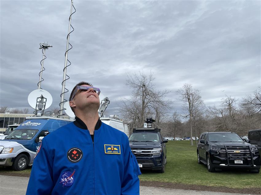Jeremy is wearing eclipse glasses and gazing up at the cloudy sky.