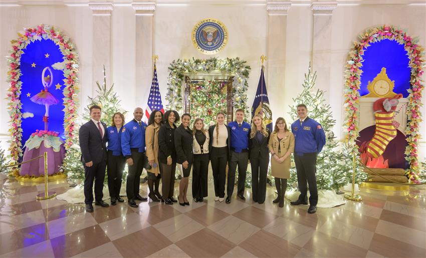 The four astronauts in their blue flight jackets posing with their family members in a large room decorated for Christma