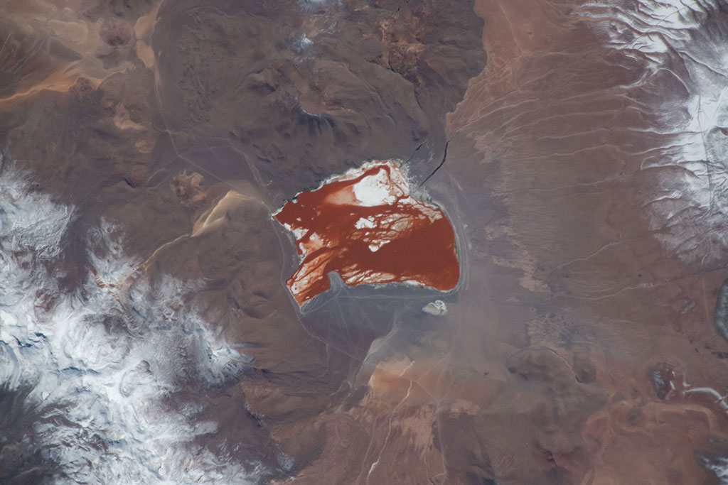 Laguna Colorada is a shallow salt lake in Bolivia, close to the border with Chile. It can easily be seen from space due the reddish color of its waters, caused by red sediments and pigmentation of some algae. The lake also contains borax islands, which appear white and contrast with the water. This photo was taken by David Saint-Jacques from the International Space Station. (Credit: Canadian Space Agency/NASA)