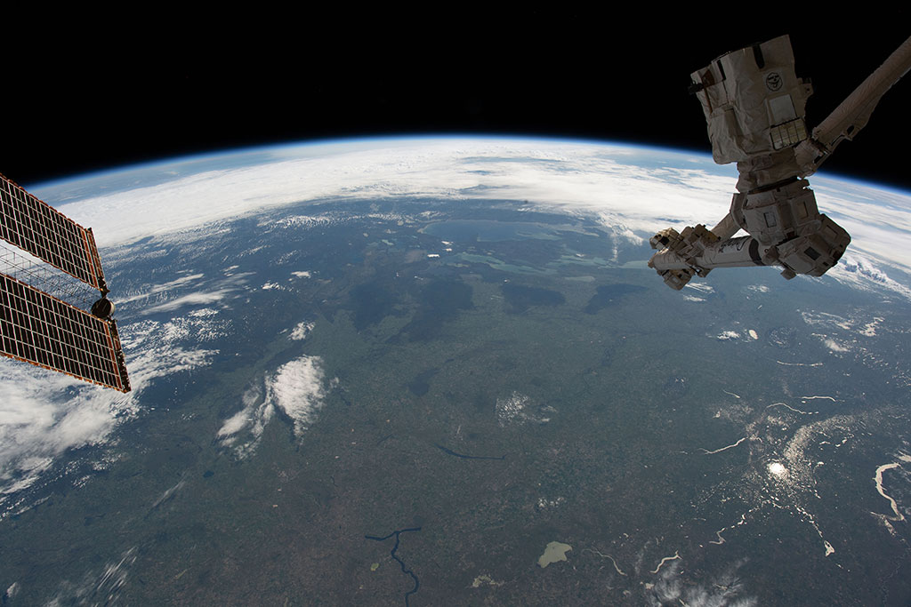 Limb of the Earth with Saskatchewan at bottom-center edge, and a lake showing the reflection of sunlight on the water. (Credit: NASA)