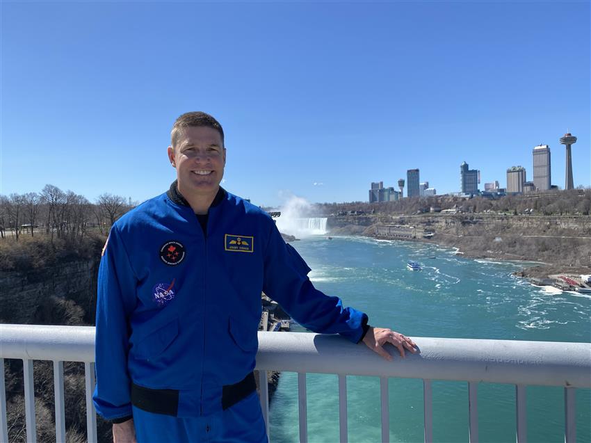 Jeremy pose sur le pont Rainbow au-dessus de la rivière Niagara. On voit les chutes derrière lui.