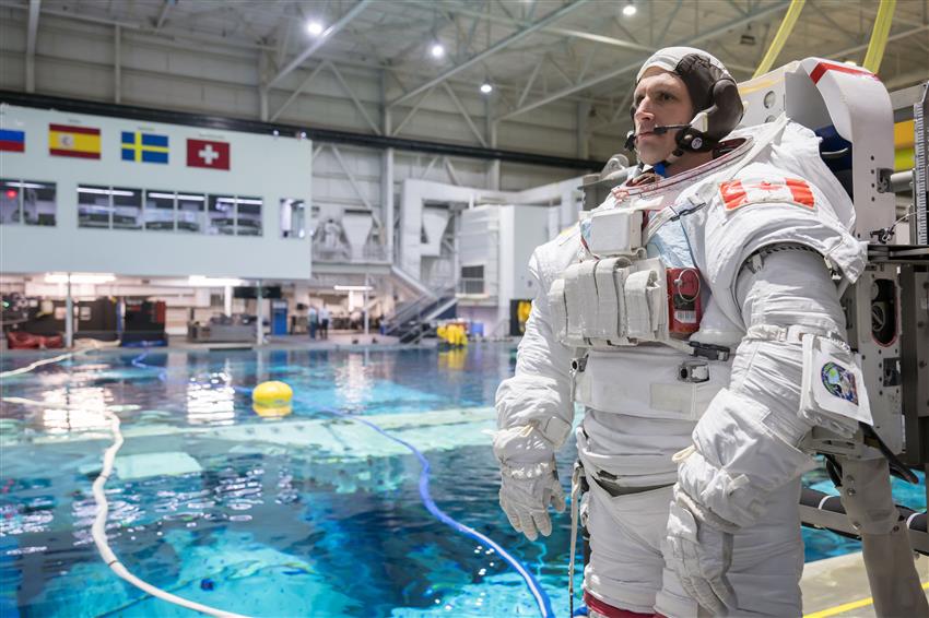 Joshua stands at the edge of a large pool, dressed in a spacesuit.