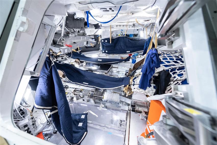 Quatre sacs de couchage accrochés aux parois d'une maquette de capsule spatiale