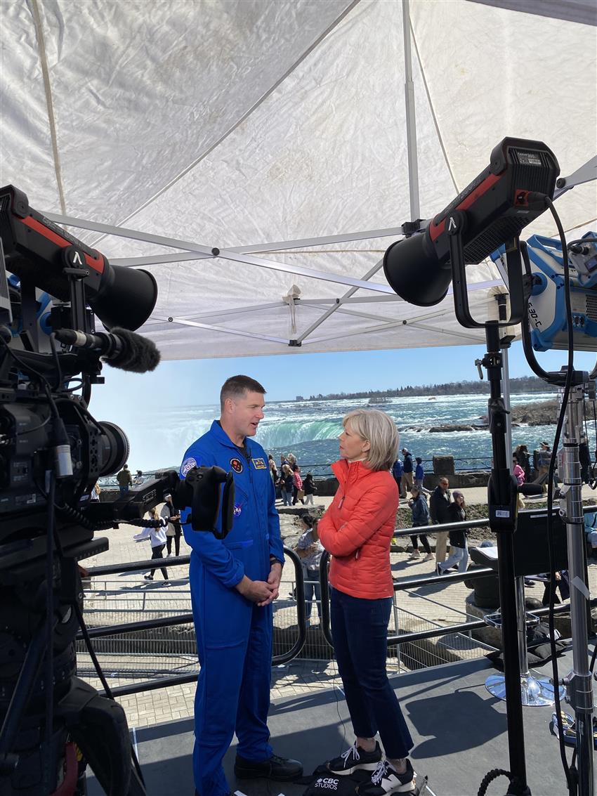 Jeremy est interviewé par les médias. On voit les chutes Niagara et un ciel bleu clair derrière lui.