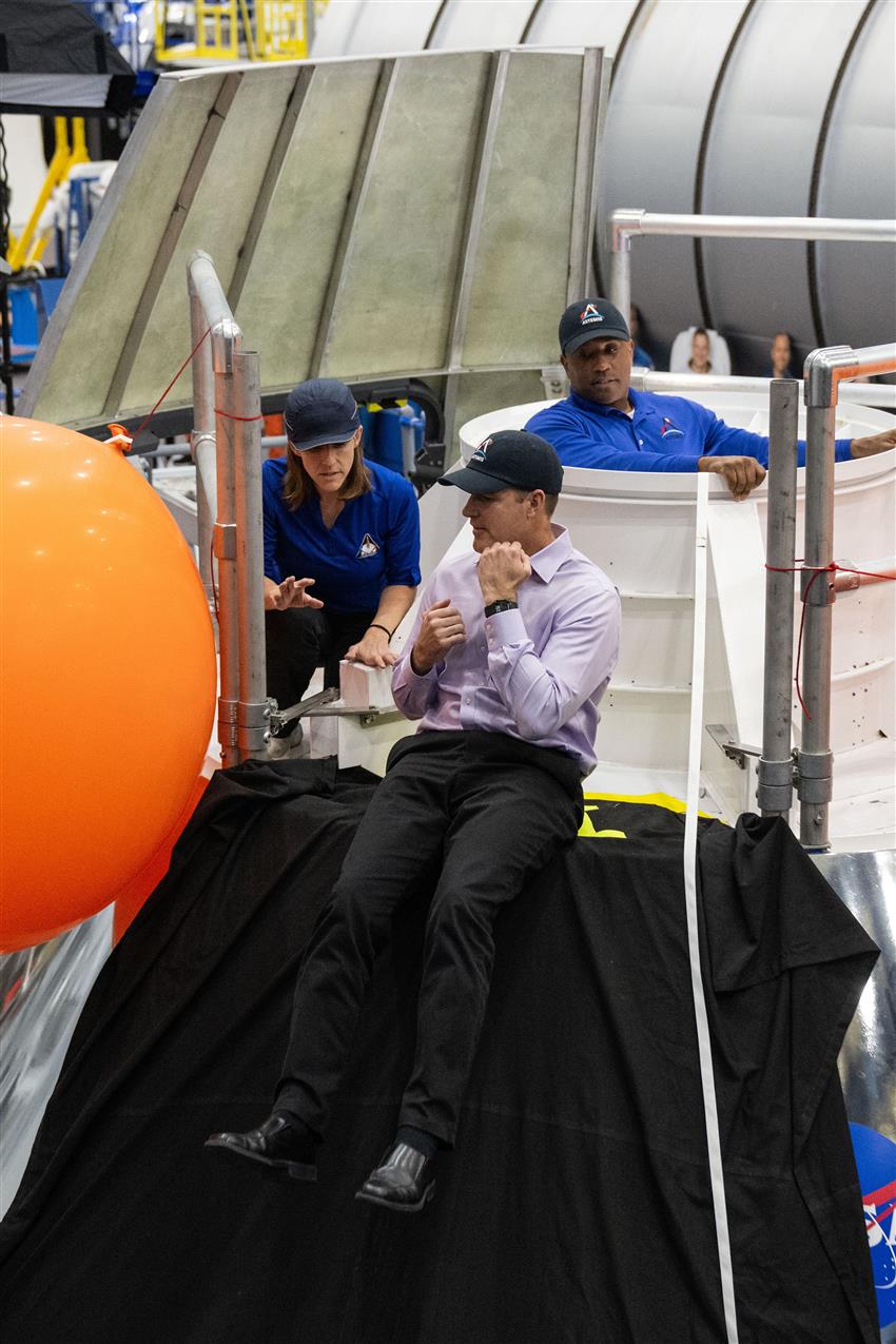 Jeremy and an individual converse atop a spacecraft slide. Victor Glover listens.