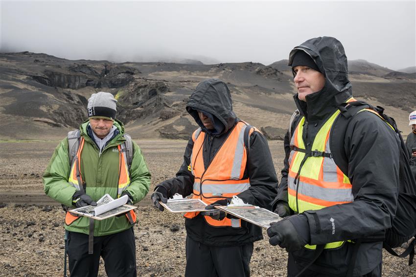 Reid, Andre et Jeremy tiennent chacun une carte du terrain et porte des dossards orange et jaune.