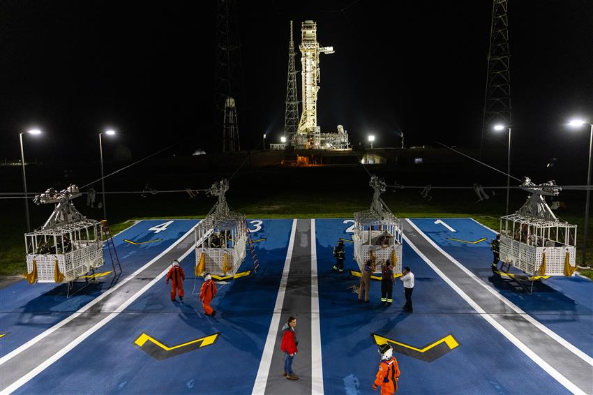 Four emergency egress baskets with people around them. A launch pad is in the background.