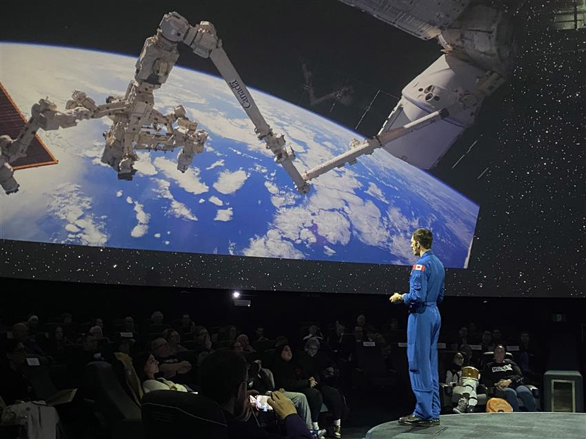 Joshua is standing in front of a large picture of Earth as seen from the International Space Station.