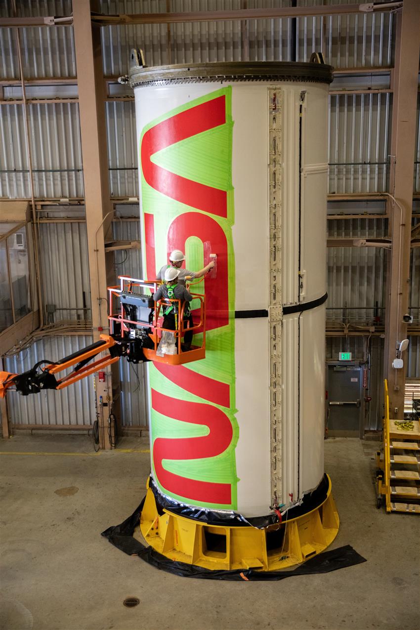 A man paints NASA logo on a large rocket in a warehouse.