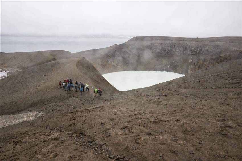 Un groupe de 17 personnes marchent sur le rebord d'une montagne rocheuse surplombant un lac.