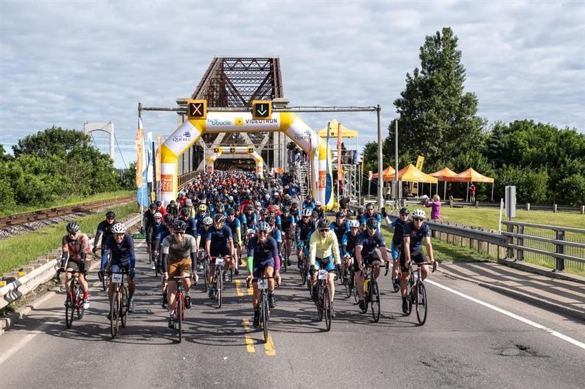 Joshua is surrounded by hundreds of cyclists and confetti with the Quebec bridge in the background.