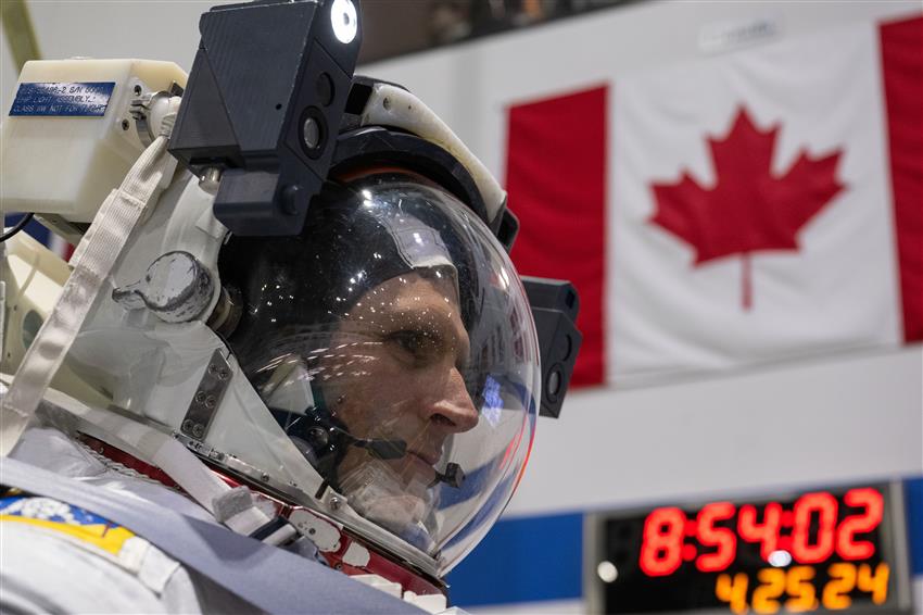 Joshua vêtu de sa combinaison spatiale devant un drapeau du Canada.