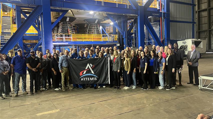 A large group of people pose in front of the core stage of the SLS rocket.