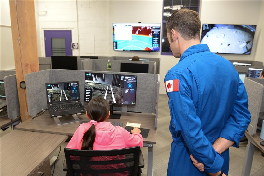 A girl and Joshua look at two screens.