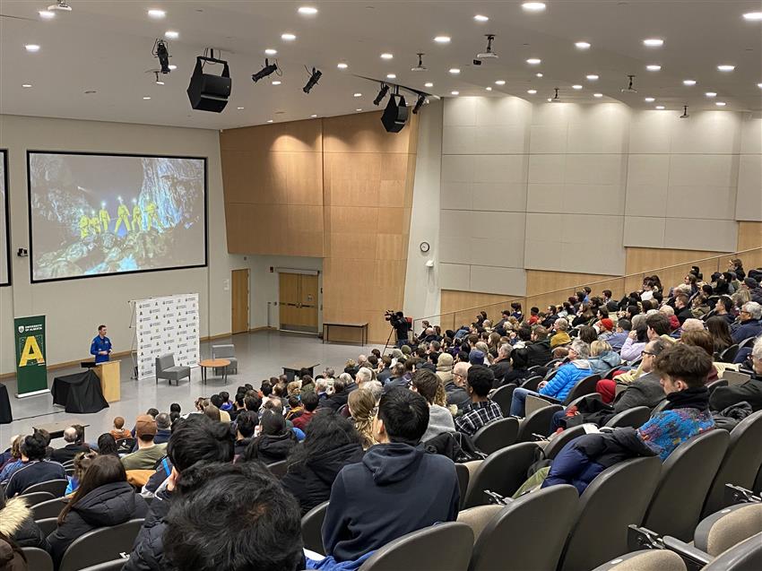 Joshua talks in a lecture hall in front of a large audience.