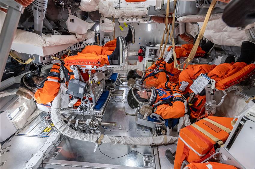 The crew in spacesuits sit horizontally with their feet raised in the Orion mockup.