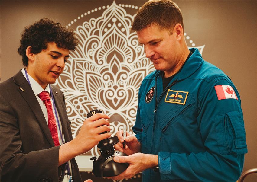 Jeremy stands with a young man while signing a joystick.