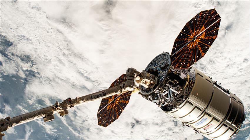 Le Canadarm2 tient Cygnus. On voit des nuages en arrière-plan.