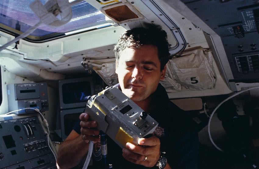 Marc is sitting on Challenger's flight deck holding a Sunphotometer.