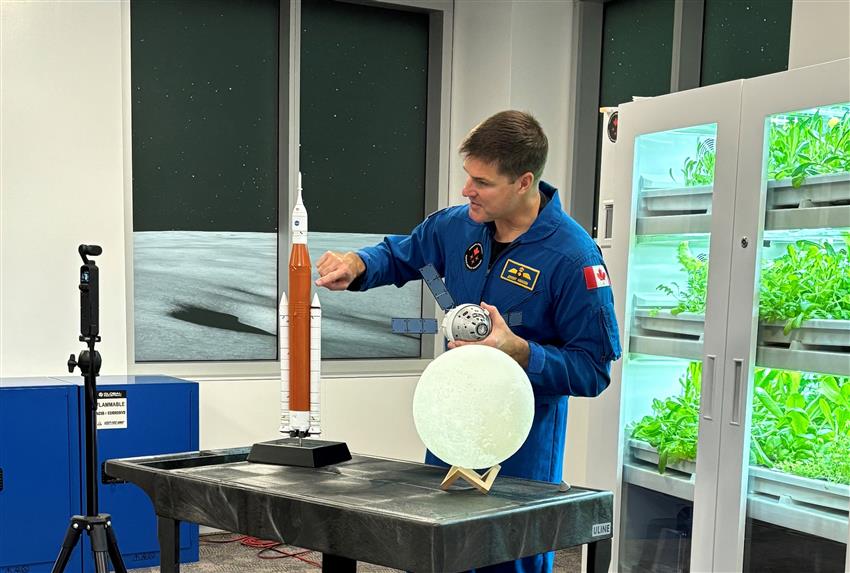 Jeremy pointe une maquette de la fusée SLS alors qu'il tient une réplique d'Orion.