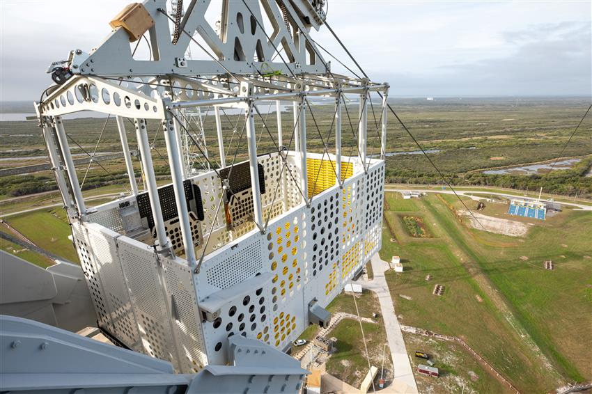 A panoramic view from a cable car, showcasing the Kennedy Space Center and the Artemis II mobile launcher below.