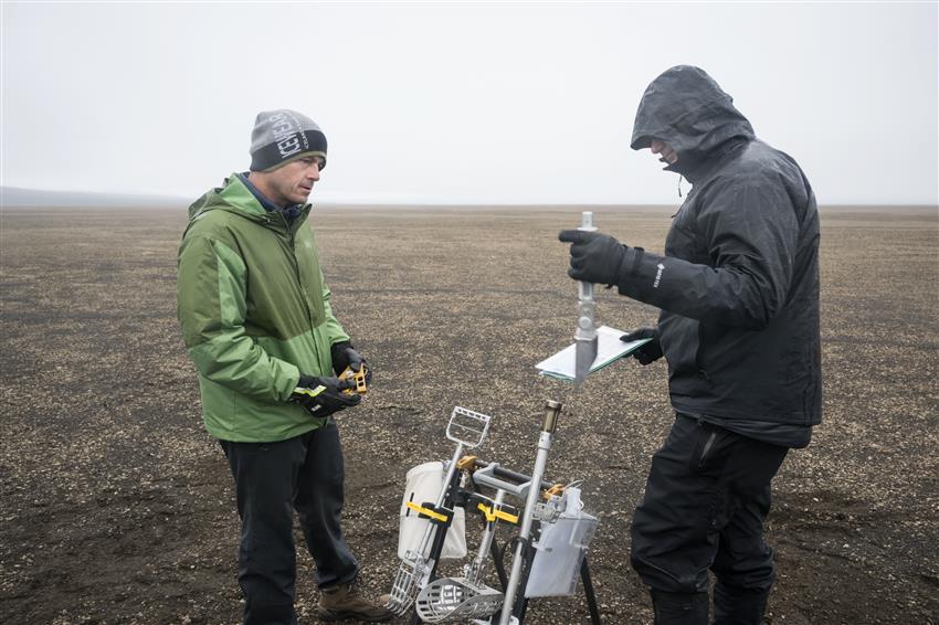 Reid and Jeremy each hold a tool, a rack with more tools between them.