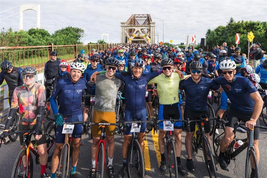 Joshua is surrounded by fellow cyclists and the Quebec bridge is visible in the background.