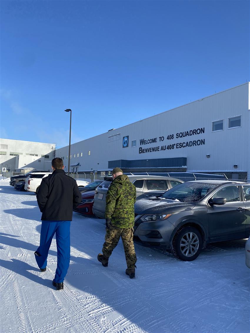 Joshua walks towards a hangar with another person.