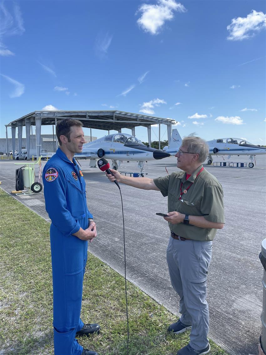 Joshua est interviewé devant deux avions à réaction.