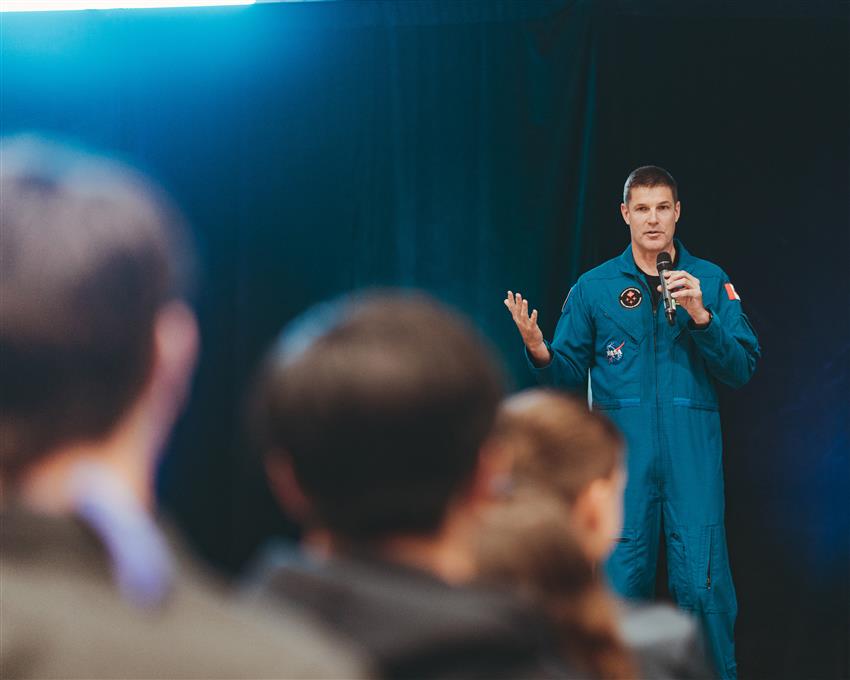 Jeremy is standing on stage and speaking into a microphone in front of an audience. 