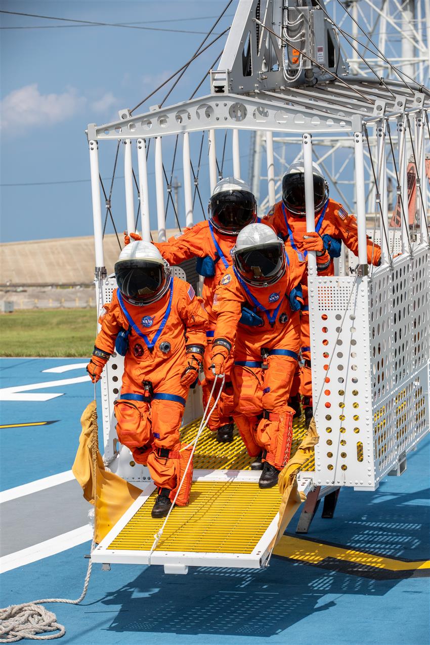 Quatre personnes portant des combinaisons de vol s'exercent à sortir d'un panier d'évacuation d'urgence.