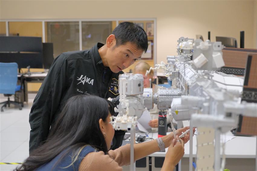 Makoto Suwa looks at a scale model of the International Space Station. Two other people are also in the photo.