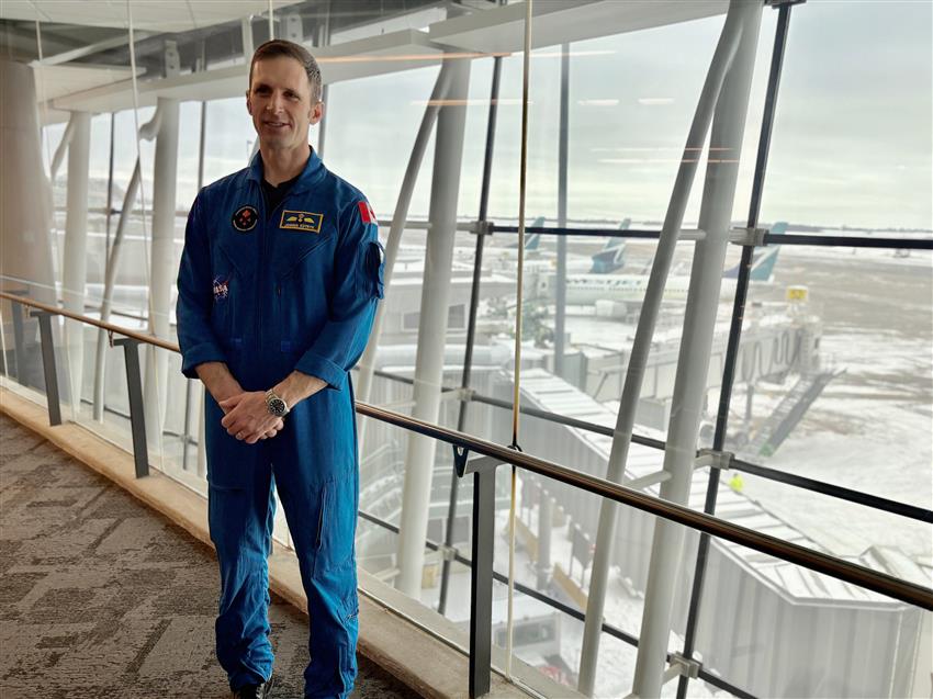 Joshua prend la pose devant une fenêtre d'un aéroport avec vue sur des avions.