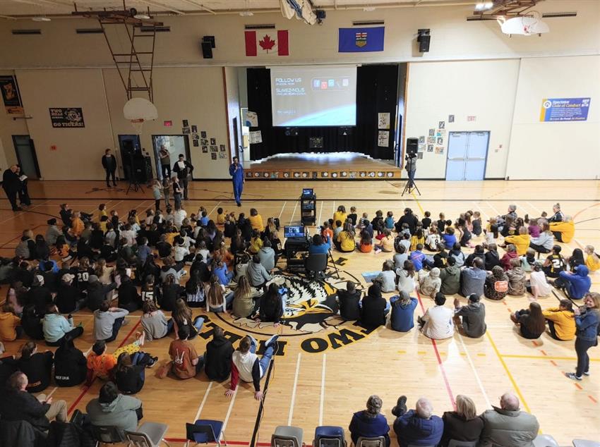 Joshua is standing in a gymnasium and speaks to students.