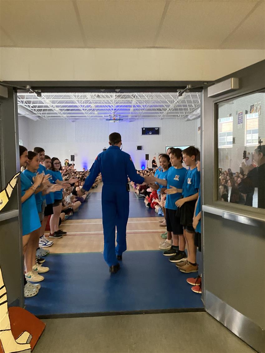 Joshua entre dans le gymnase d'une école. Des élèves font une haie d'honneur. 