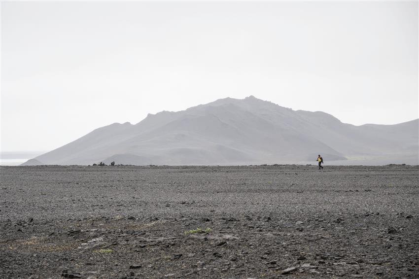 Jeremy, portant un dossard orange et jaune, marche au loin dans un desert rocailleux.