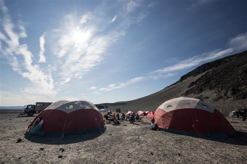 People sit on camping chairs surrounded by red and white tents.